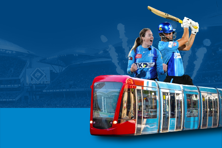 Two Adelaide Strikers players in action with Adelaide Oval in the background and a tram in front.