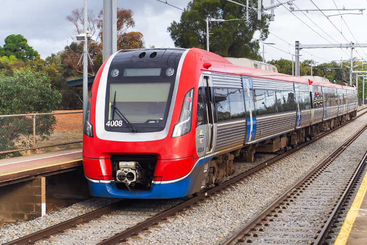 An Adelaide Metro train travelling on a rail line passing through a station.